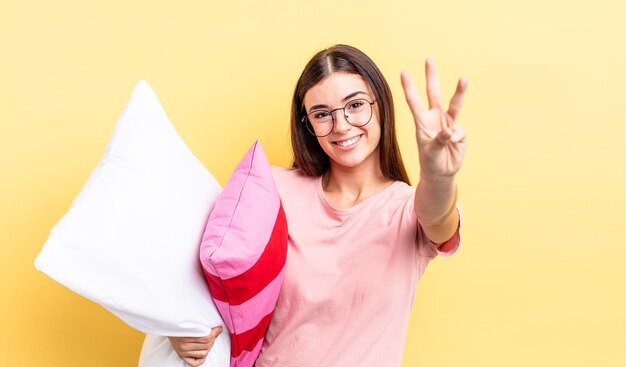 Giovane donna ispanica sorridente e dall'aspetto amichevole che mostra il concetto di pigiama e cuscino numero tre