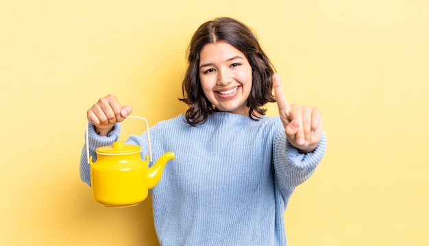 Giovane donna ispanica sorridente e dall'aspetto amichevole che mostra il concetto di teiera numero uno