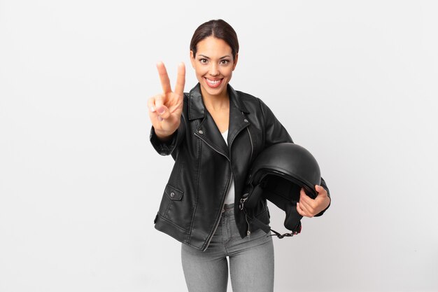 giovane donna ispanica sorridente e dall'aspetto amichevole, mostrando il numero due. concetto di motociclista