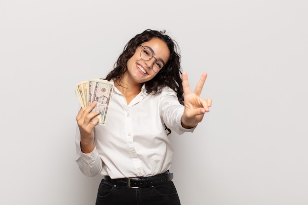 Giovane donna ispanica sorridente e dall'aspetto amichevole, mostrando il numero due o il secondo con la mano in avanti, il conto alla rovescia