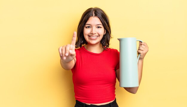 Giovane donna ispanica sorridente e dall'aspetto amichevole, mostrando il numero uno. concetto di thermos