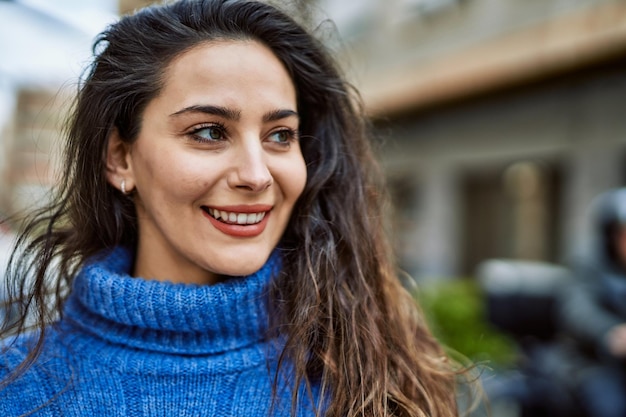 Giovane donna ispanica sorridente felice in piedi in città.