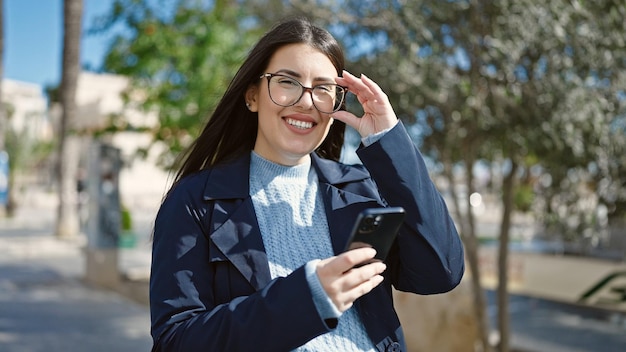 Giovane donna ispanica sorridente fiducioso utilizzando lo smartphone al parco