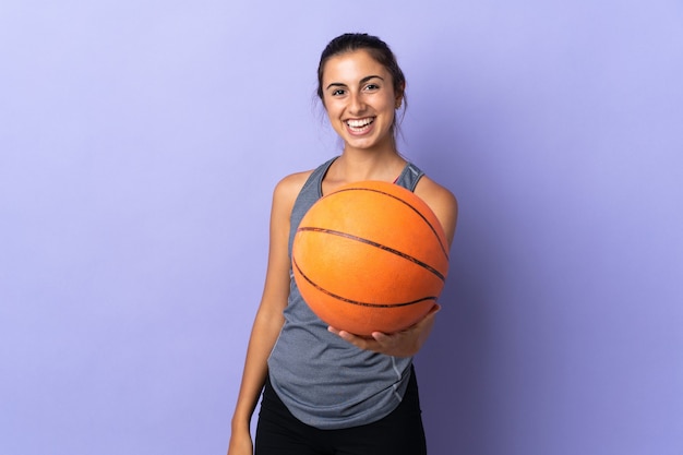 Giovane donna ispanica su sfondo viola isolato giocando a basket