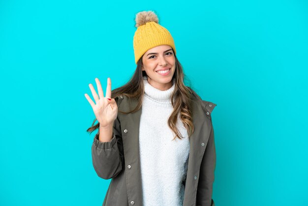 Giovane donna italiana che indossa giacca invernale e cappello isolati su sfondo blu felice e contando quattro con le dita