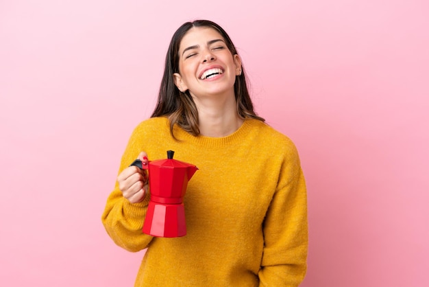 Giovane donna italiana che tiene una caffettiera isolata su sfondo rosa ridendo