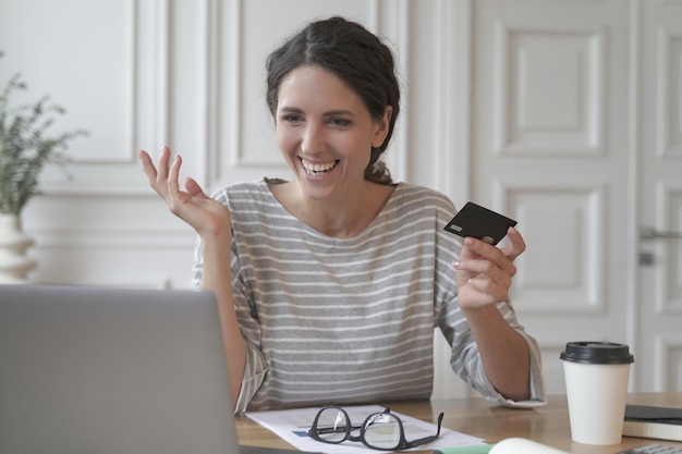 Giovane donna italiana sorridente che effettua il pagamento con carta di plastica durante lo shopping online sul laptop