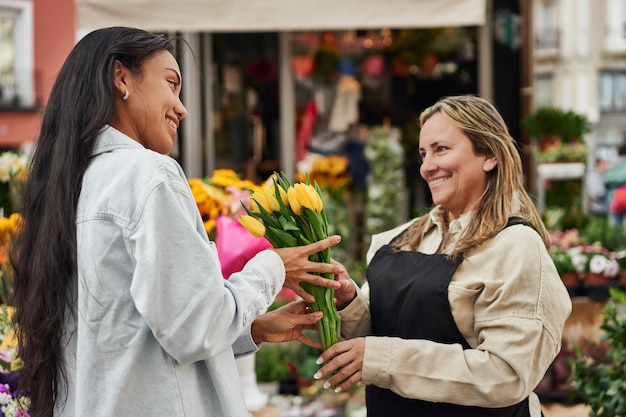 Giovane donna latina che acquista fiori vivaci dalla bancarella di un venditore ambulante consegnata dal giardiniere