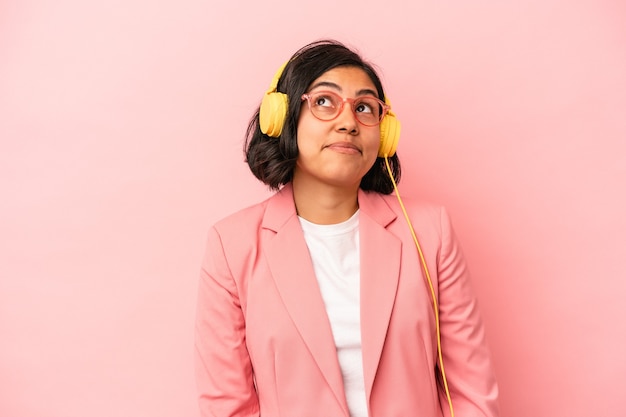 Giovane donna latina che ascolta musica isolata su sfondo rosa sognando di raggiungere obiettivi e scopi