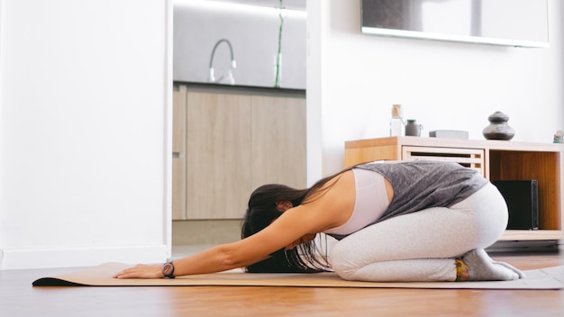 Giovane donna latina che fa balasana posa yoga su un tappetino nel suo soggiorno Copia spazio