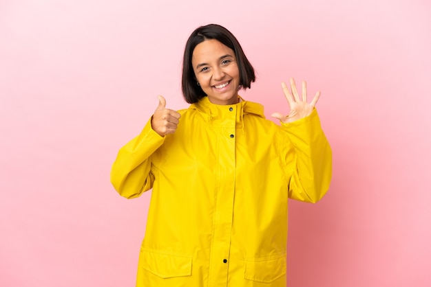 Giovane donna latina che indossa un cappotto antipioggia su sfondo isolato contando sei con le dita