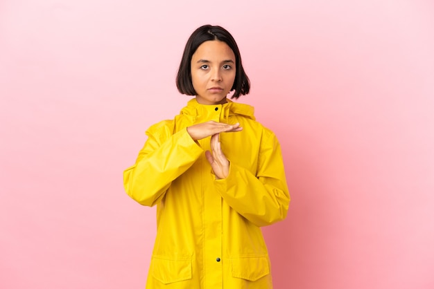 Giovane donna latina che indossa un cappotto antipioggia su sfondo isolato facendo un gesto di time out time