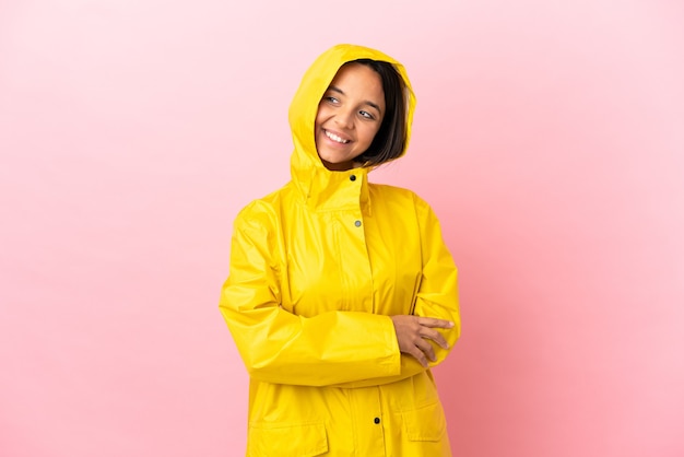 Giovane donna latina che indossa un cappotto antipioggia su sfondo isolato guardando di lato e sorridente