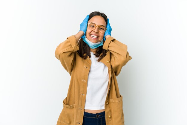 Giovane donna latina che indossa una maschera per proteggersi dalle risate isolate covid mantenendo con gioia le mani sulla testa. Concetto di felicità.