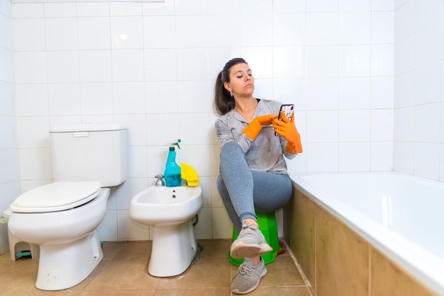 Giovane donna latina che pulisce il bagno giocando con il cellulare