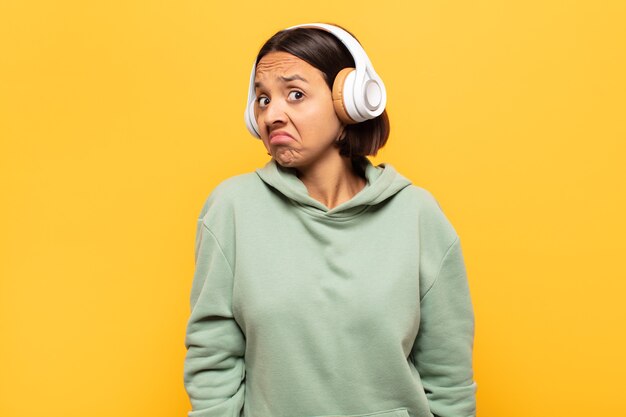 Giovane donna latina che scrolla le spalle, sentendosi confusa e incerta, dubbiosa con le braccia incrociate e lo sguardo perplesso