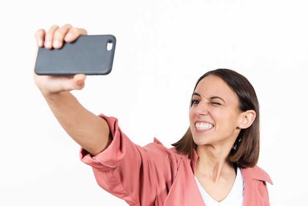 Giovane donna latina che si fa un selfie mentre strizza l'occhio su sfondo bianco.