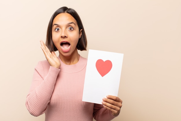 Giovane donna latina che si sente felice, eccitata, sorpresa o scioccata, sorridente e stupita per qualcosa di incredibile