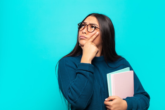 Giovane donna latina che si sente premurosa, si chiede o immagina idee, sogna ad occhi aperti e alza lo sguardo per copiare lo spazio