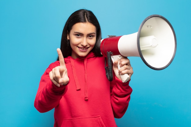 Giovane donna latina che sorride con orgoglio e sicurezza facendo la posa numero uno in modo trionfante, sentendosi come un leader