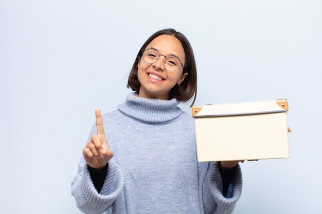 Giovane donna latina che sorride con orgoglio e sicurezza mentre posa trionfante il numero uno, sentendosi come un leader