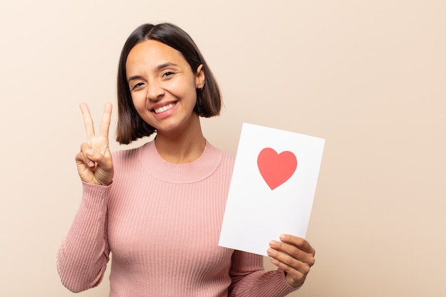 Giovane donna latina che sorride e sembra amichevole, mostrando il numero due o il secondo con la mano in avanti, contando alla rovescia