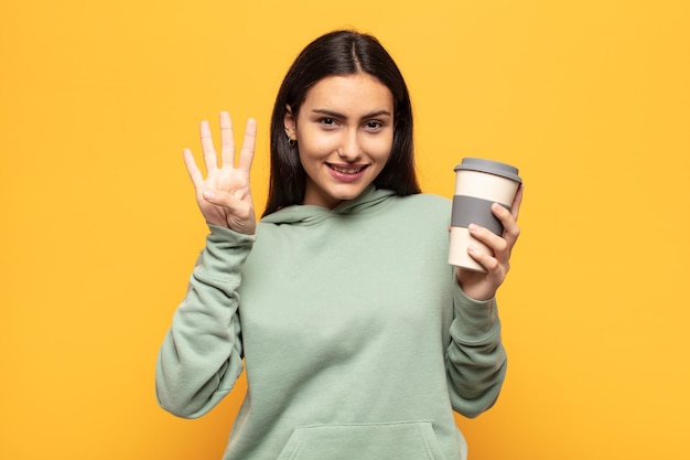 Giovane donna latina che sorride e sembra amichevole, mostrando il numero quattro o quarto con la mano in avanti, contando alla rovescia