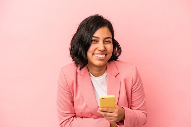 Giovane donna latina che tiene il telefono cellulare isolato su sfondo rosa ridendo e divertendosi.