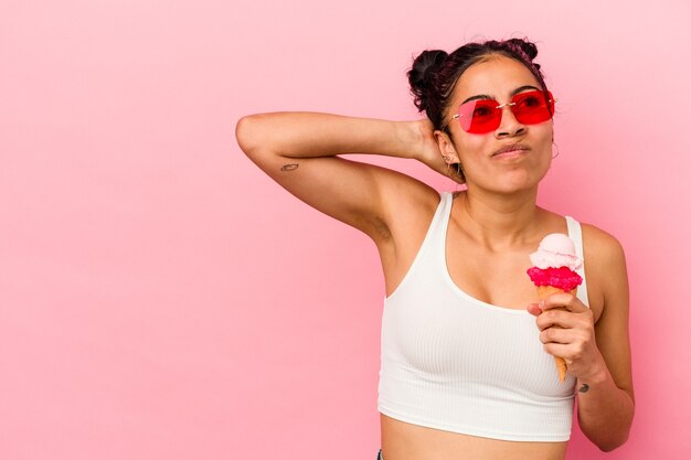 Giovane donna latina che tiene un gelato isolato su sfondo rosa toccando la parte posteriore della testa, pensando e facendo una scelta.