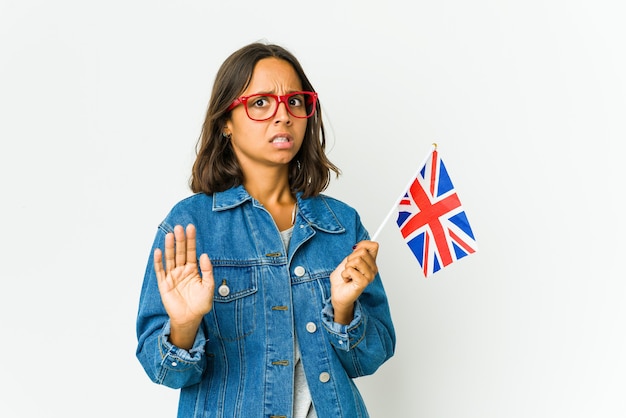 Giovane donna latina che tiene una bandiera inglese isolata su bianco che rifiuta qualcuno che mostra un gesto di disgusto.