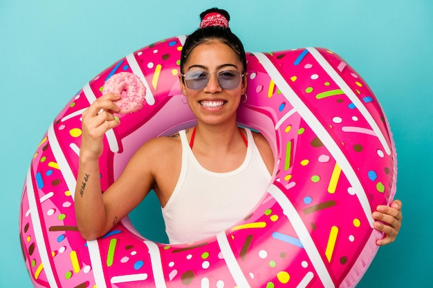 Giovane donna latina che tiene una ciambella gonfiabile che mangia una ciambella isolata su priorità bassa blu