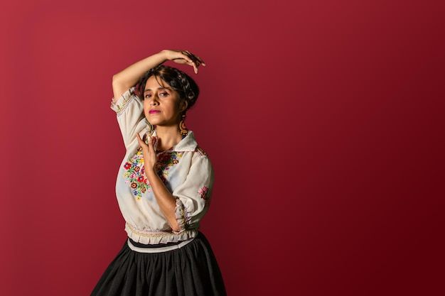 Giovane donna latina con abito tradizionale di camicetta e gonna mentre si posa con le mani in posizione di danza su uno sfondo marrone Copia spazio