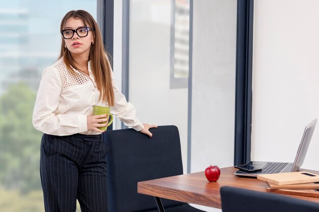 Giovane donna latina con una tazza di caffè in mano che si prende una pausa mentre lavora a casa