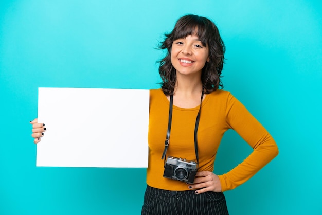 Giovane donna latina del fotografo isolata su fondo blu che tiene un cartello vuoto con l'espressione felice