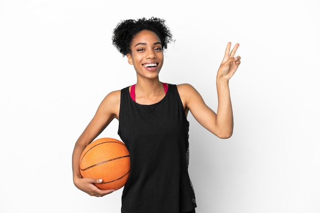 Giovane donna latina del giocatore di pallacanestro isolata su fondo bianco che sorride e che mostra il segno di vittoria