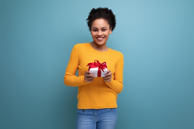 Giovane donna latina felice con capelli afro che tiene confezione regalo su sfondo studio