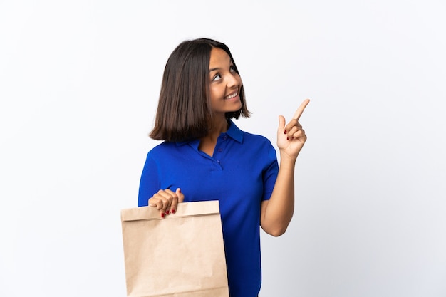 Giovane donna latina in possesso di un sacchetto della spesa isolato su bianco che punta con il dito indice una grande idea