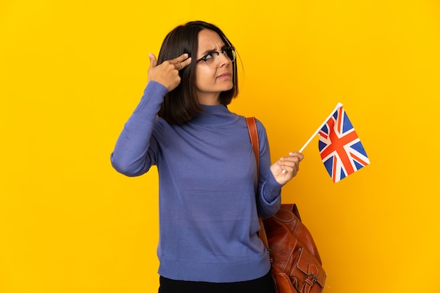 Giovane donna latina in possesso di una bandiera del Regno Unito isolata su sfondo giallo con problemi a compiere gesti suicidi