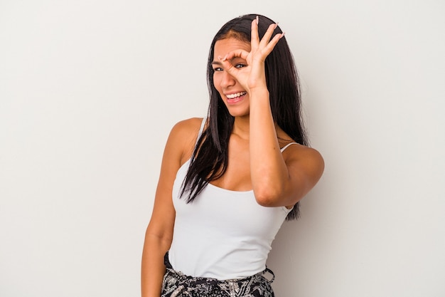 Giovane donna latina isolata su sfondo bianco eccitato mantenendo il gesto ok sull'occhio.