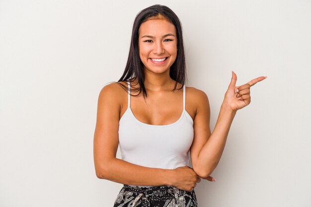 Giovane donna latina isolata su sfondo bianco sorridente allegramente che punta con l'indice lontano.