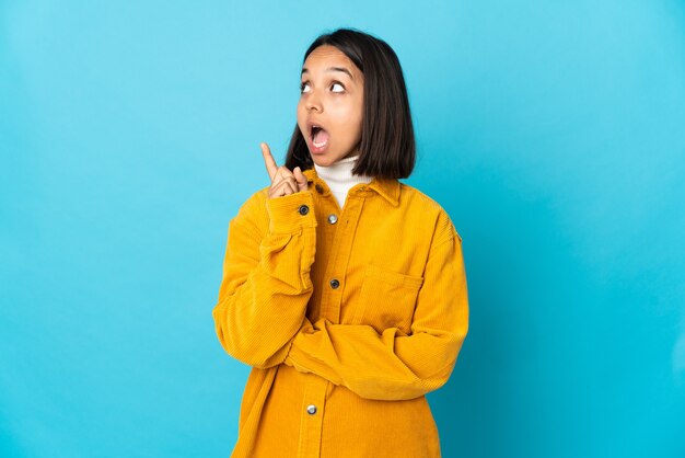 Giovane donna latina isolata su sfondo blu pensando un'idea puntando il dito verso l'alto