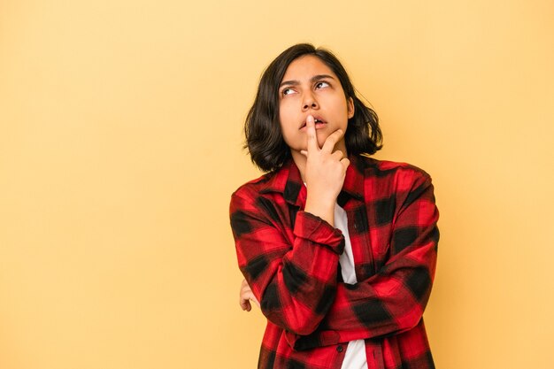 Giovane donna latina isolata su sfondo giallo guardando lateralmente con espressione dubbiosa e scettica.