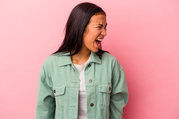 Giovane donna latina isolata su sfondo rosa che grida molto arrabbiato, concetto di rabbia, frustrato.