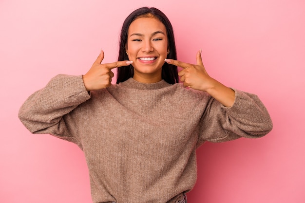 Giovane donna latina isolata su sfondo rosa sorride, puntando il dito alla bocca.