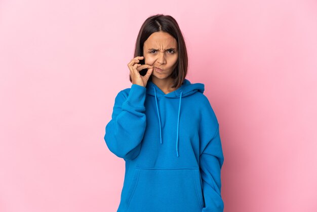 Giovane donna latina isolata sulla parete rosa che mostra un segno del gesto di silenzio