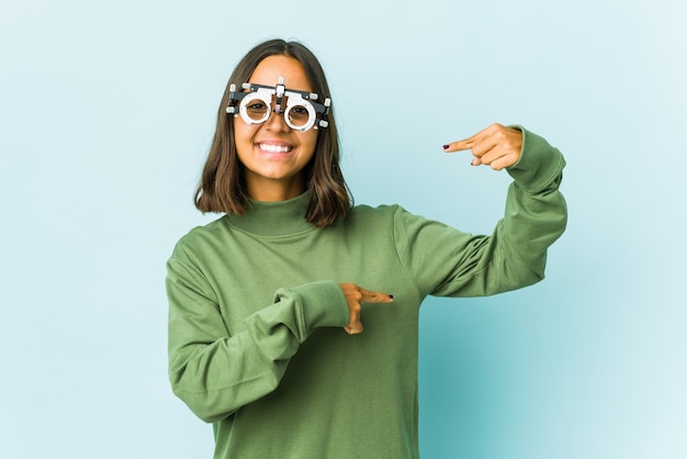 Giovane donna latina oculista che tiene qualcosa di piccolo con gli indici, sorridente e sicura.