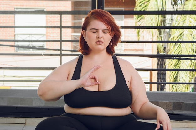 Giovane donna latina plus size che medita con la mano sul petto in posizione gyan mudra