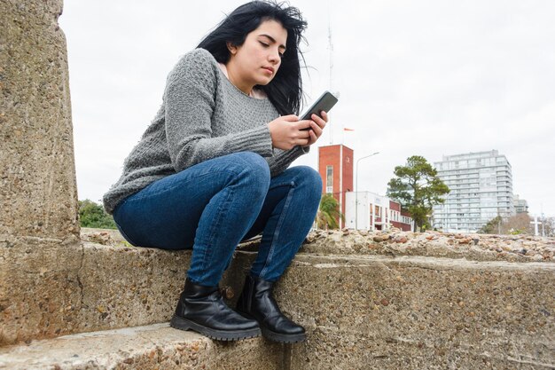 giovane donna latina seduta all'aperto concentrata controllando seriamente lo spazio della copia del telefono