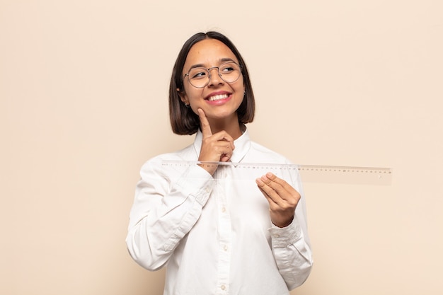 Giovane donna latina sorridente felicemente e fantasticando o dubitando, guardando al lato