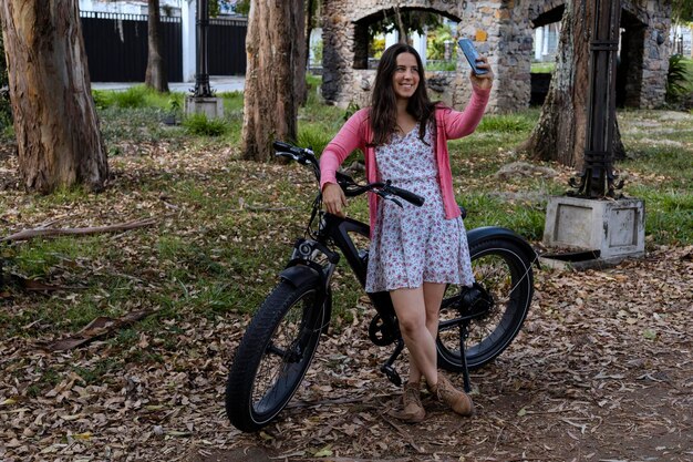 Giovane donna latinoamericana 33 in un giro primaverile con la sua bicicletta elettrica sta usando il suo telefono cellulare per un autoritratto Concept mezzo di trasporto e primavera